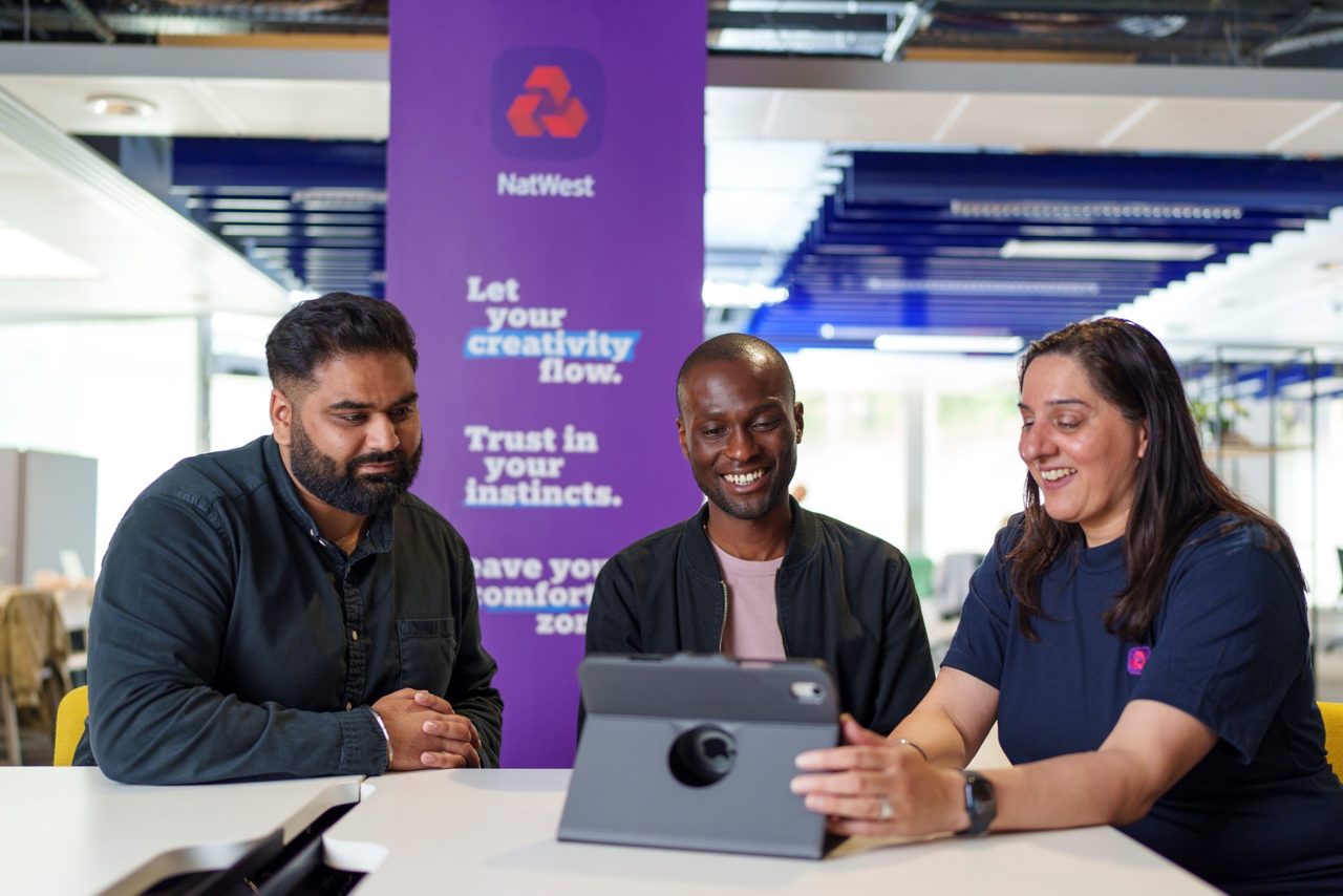 This images shows three people, two male and a female in our Accelerator hub in Birmingham. They are sat at a table looking at a tablet. 