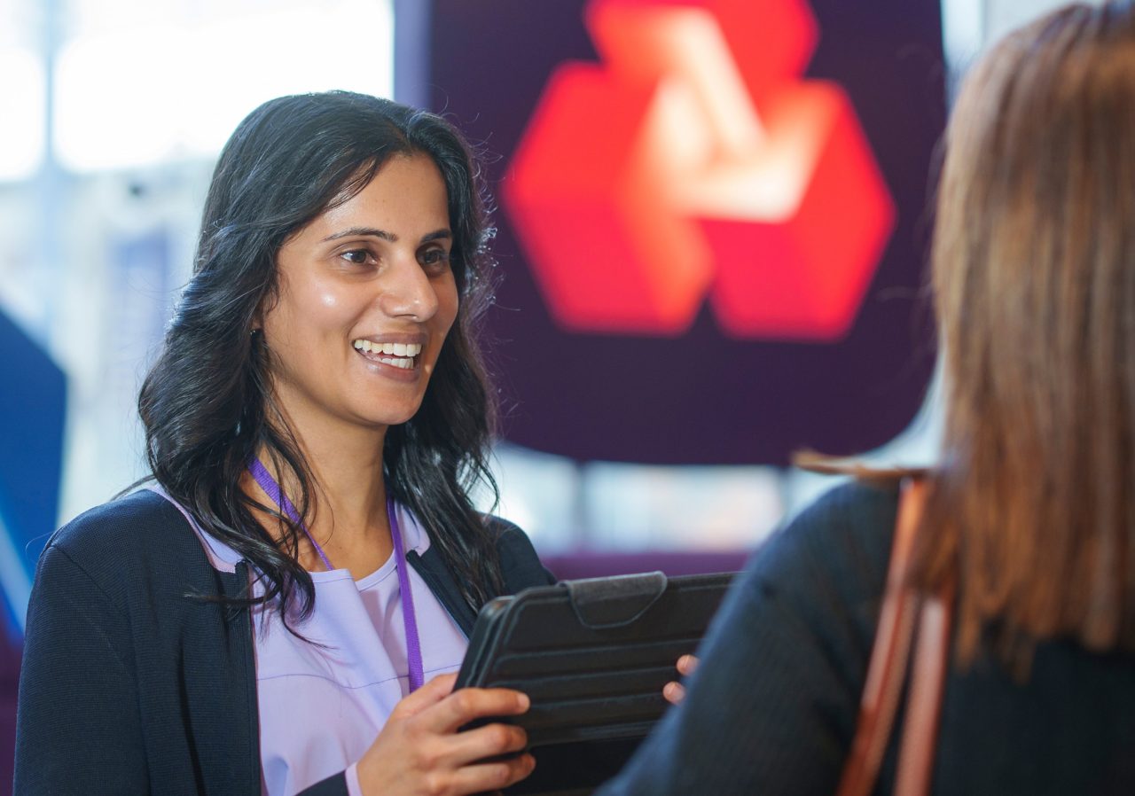 This image shows a female NatWest colleague in a branch talking with a customer. 