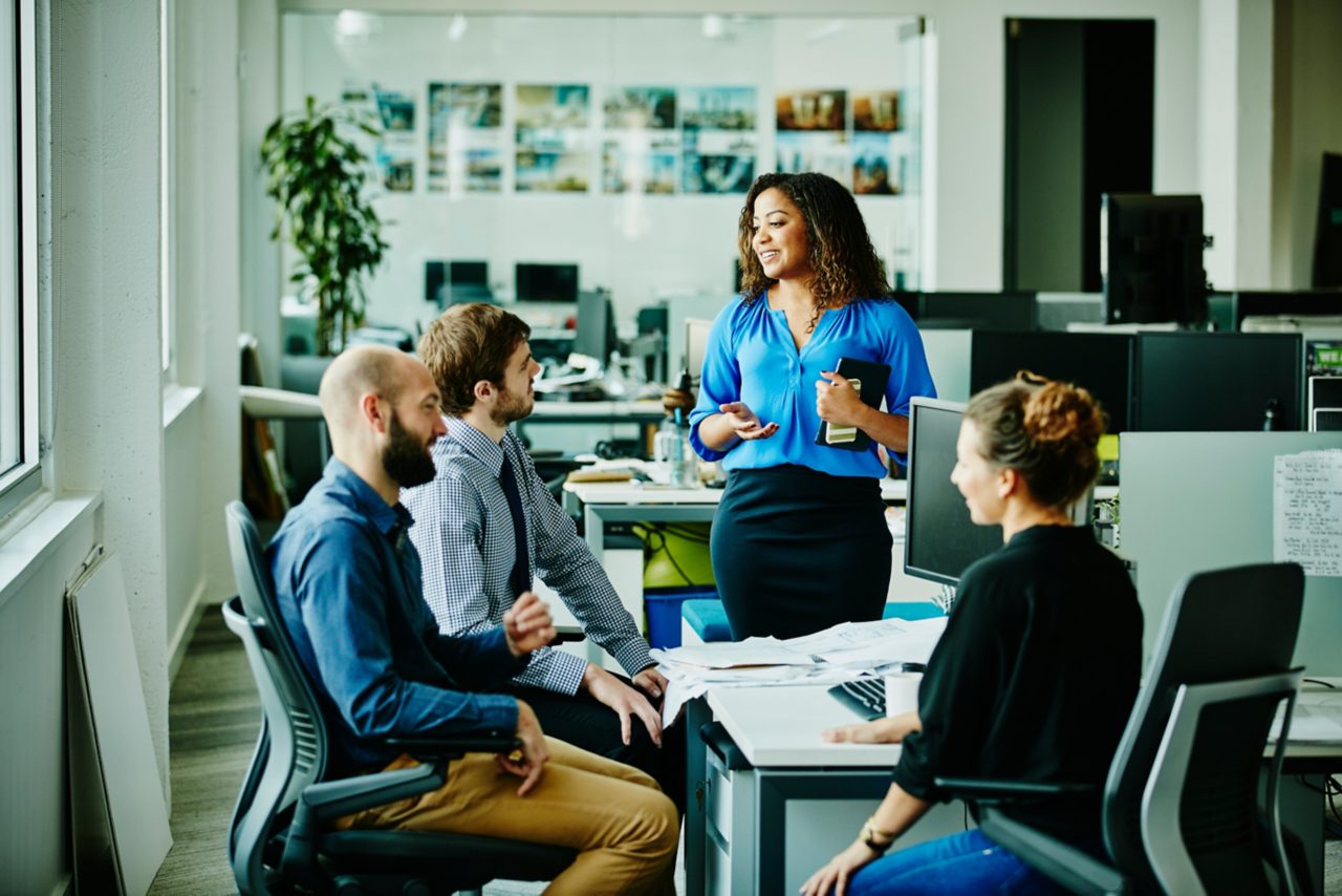 Image of a businesswoman leading meeting with colleagues at office workstation