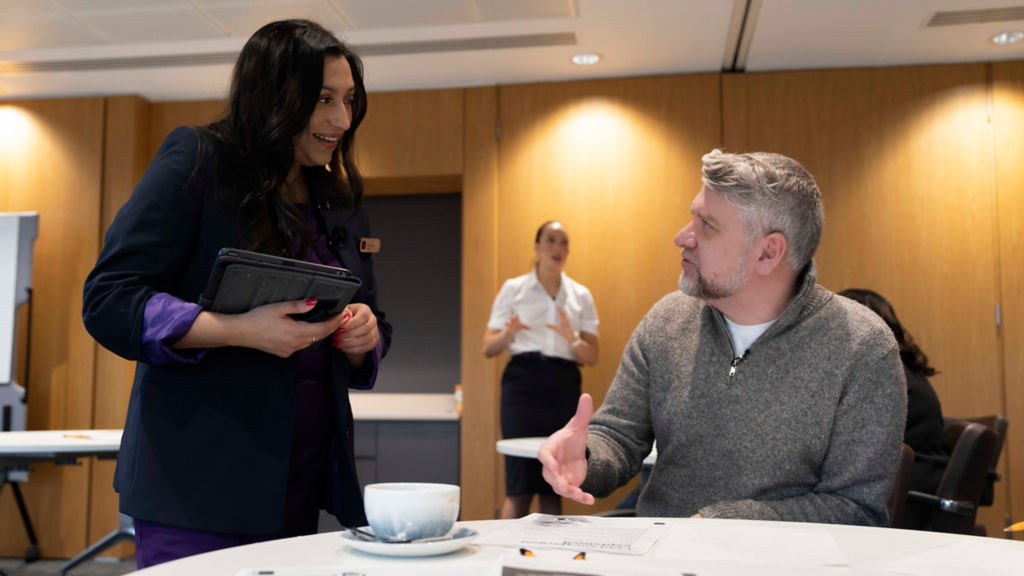 This image shows a female standing up talking to a man who is sitting down. 