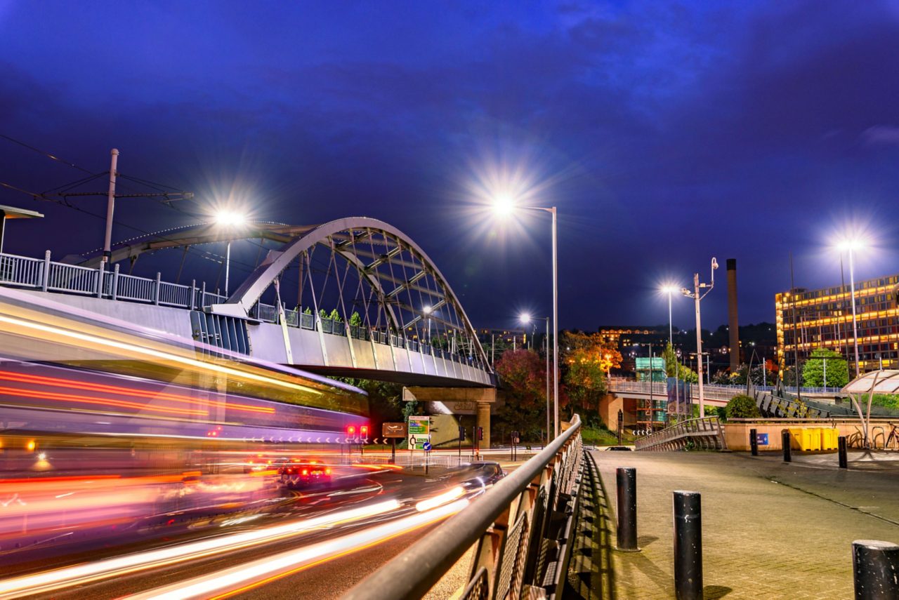 Night view of Sheffield featuring the illuminated Park Square Bridge with light trails from traffic and city buildings in the background