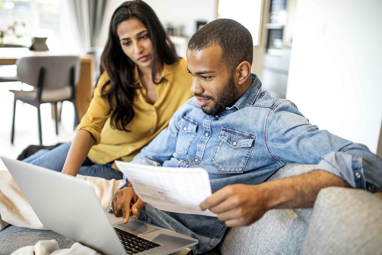 Couple on sofa looking at laptop and paperwork